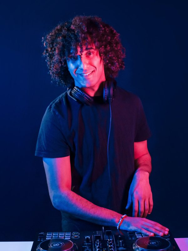 man-with-curly-hair-using-dj-equipment-and-standing-in-the-dark-neon-lighted-room.jpg